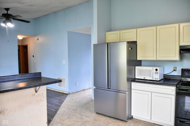 kitchen featuring freestanding refrigerator, electric range, dark countertops, white microwave, and cream cabinets