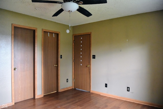 unfurnished bedroom with baseboards, multiple closets, ceiling fan, and wood finished floors