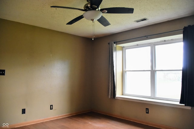 empty room featuring ceiling fan, a textured ceiling, light wood-style flooring, baseboards, and visible vents