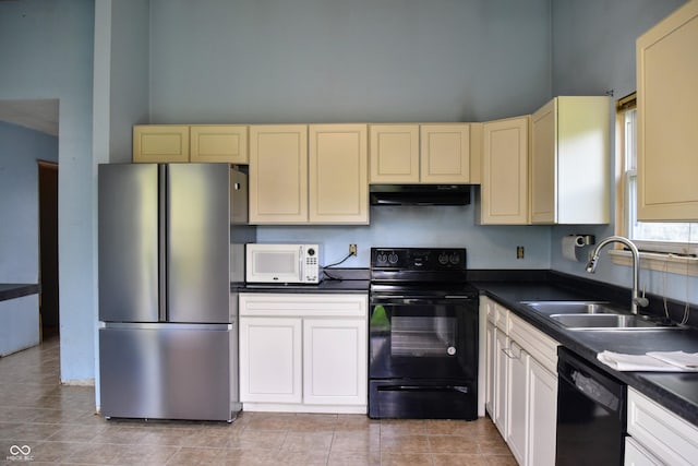 kitchen with a towering ceiling, a sink, black appliances, under cabinet range hood, and cream cabinetry
