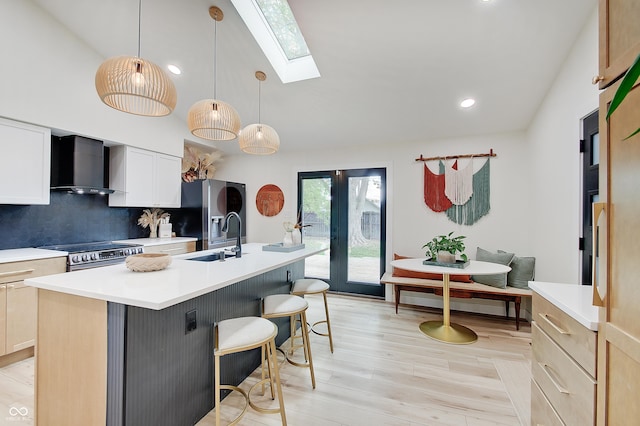 kitchen with wall chimney exhaust hood, a sink, stainless steel appliances, a skylight, and an island with sink