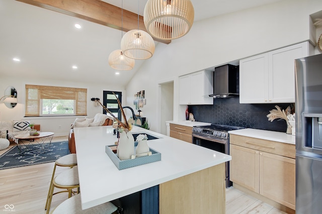 kitchen with appliances with stainless steel finishes, wall chimney range hood, light wood-style flooring, open floor plan, and a breakfast bar