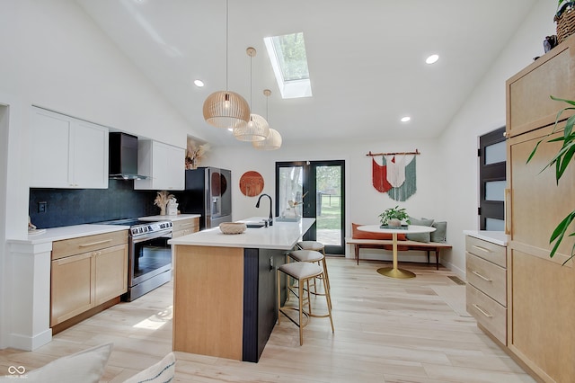 kitchen with appliances with stainless steel finishes, wall chimney exhaust hood, a skylight, decorative backsplash, and high vaulted ceiling