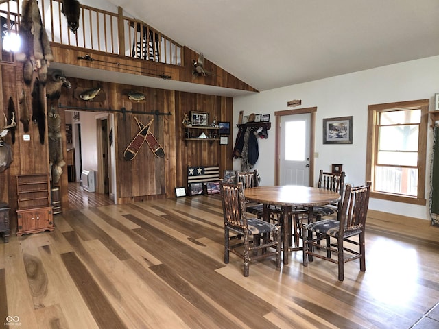 dining space featuring wood finished floors, wood walls, and high vaulted ceiling