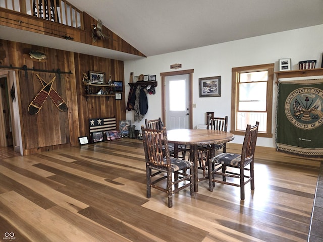 dining area with wood finished floors, a barn door, wood walls, and high vaulted ceiling