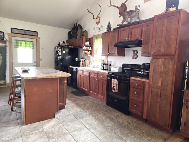 kitchen featuring black appliances, under cabinet range hood, healthy amount of natural light, vaulted ceiling, and a center island