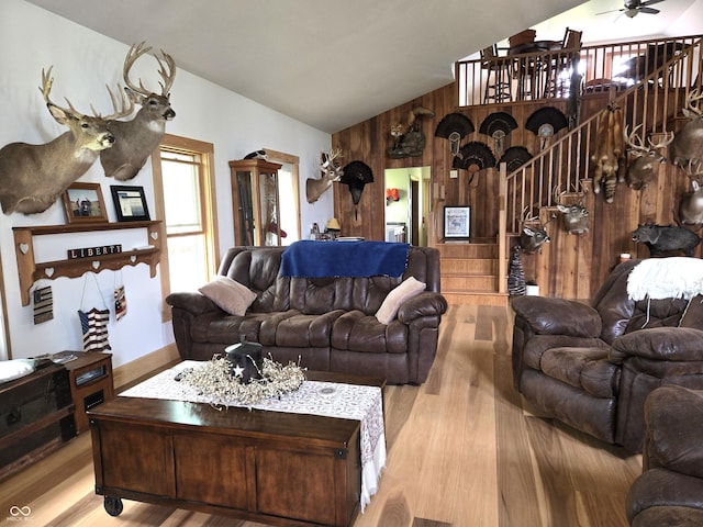 living room with lofted ceiling, stairway, wood walls, wood finished floors, and a ceiling fan