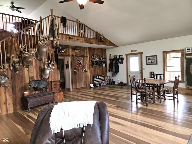 living area with ceiling fan, wood finished floors, high vaulted ceiling, and wooden walls