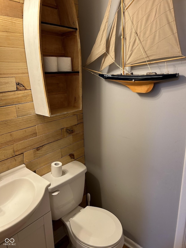 half bath featuring wooden walls, vanity, and toilet