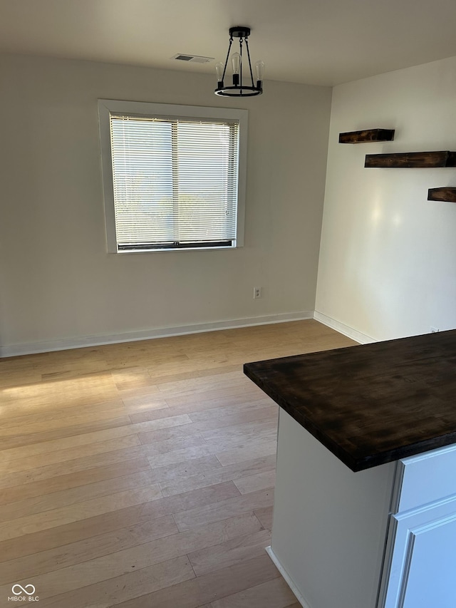 unfurnished dining area with baseboards, a notable chandelier, light wood-style flooring, and visible vents
