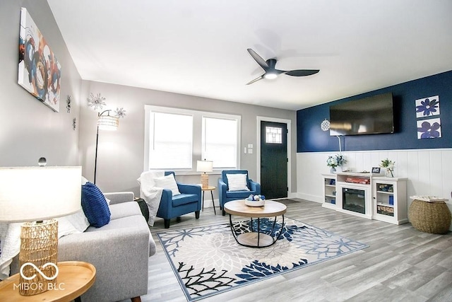 living area featuring a wainscoted wall, a ceiling fan, and wood finished floors
