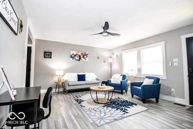 living area with baseboards, a ceiling fan, light wood finished floors, and visible vents