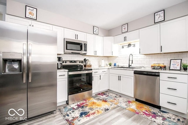 kitchen with appliances with stainless steel finishes, tasteful backsplash, a sink, white cabinets, and light wood-style floors