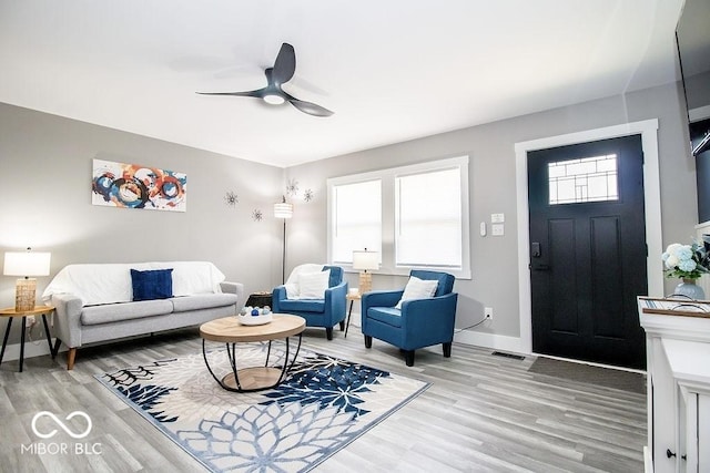living room featuring baseboards, a ceiling fan, light wood-style flooring, and visible vents