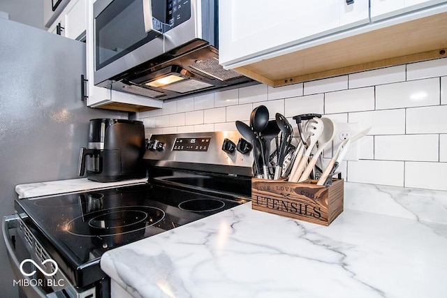kitchen with backsplash, white cabinets, light stone countertops, and stainless steel appliances