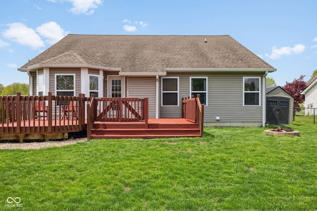 rear view of house featuring a storage unit, a shingled roof, a wooden deck, an outbuilding, and a lawn