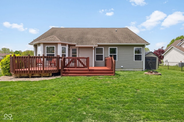 rear view of house featuring fence, a shingled roof, a storage shed, a wooden deck, and a lawn