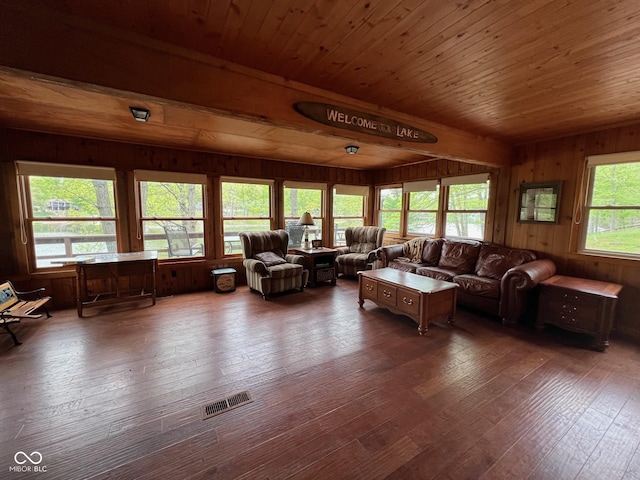 living room featuring wood-type flooring, wood walls, wooden ceiling, and visible vents