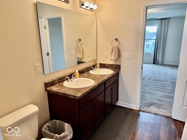 full bath with double vanity, wood finished floors, a sink, baseboards, and toilet