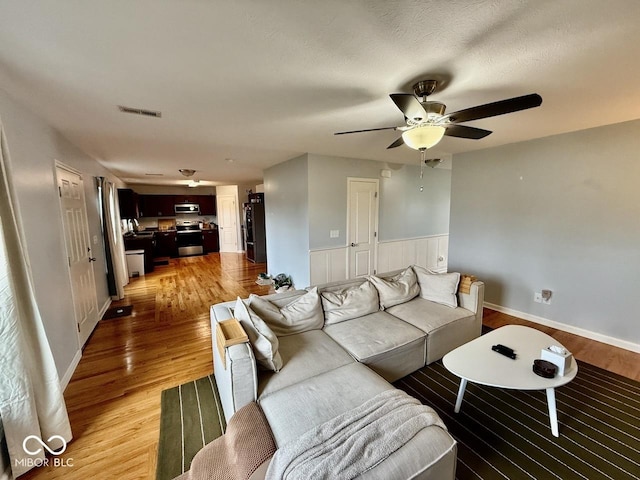 living area featuring visible vents, a ceiling fan, light wood-style flooring, and wainscoting
