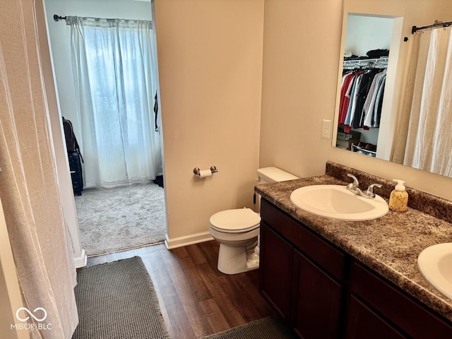 bathroom featuring a sink, double vanity, toilet, and wood finished floors