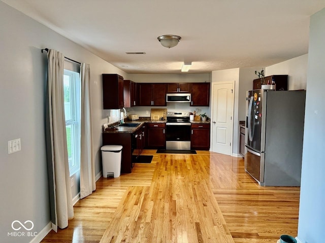kitchen featuring a sink, stainless steel appliances, baseboards, light wood-type flooring, and visible vents