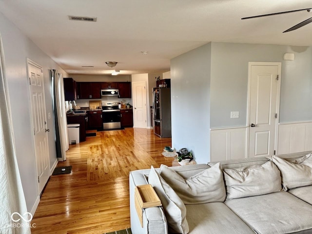 living room featuring light wood-style floors, wainscoting, and ceiling fan