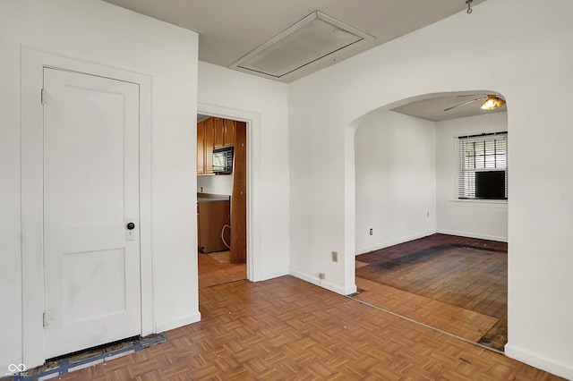unfurnished room with baseboards, attic access, and arched walkways