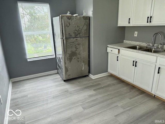 kitchen featuring freestanding refrigerator, white cabinetry, a sink, and light wood-style flooring
