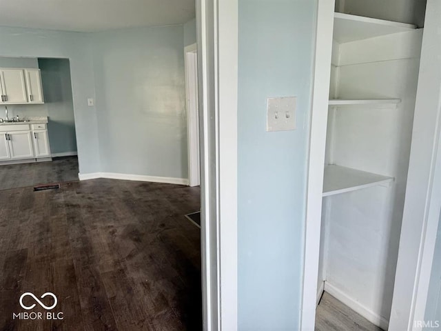 hallway with baseboards, dark wood-style floors, and a sink