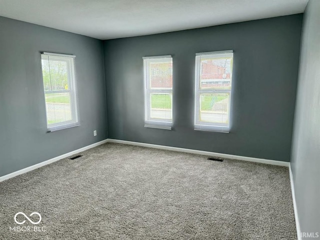 carpeted spare room featuring a healthy amount of sunlight, baseboards, and visible vents