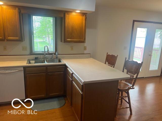 kitchen featuring a peninsula, a breakfast bar, white dishwasher, light countertops, and a sink