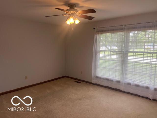 spare room with baseboards, ceiling fan, visible vents, and light carpet