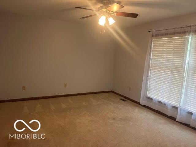 empty room with baseboards, visible vents, a ceiling fan, and light colored carpet