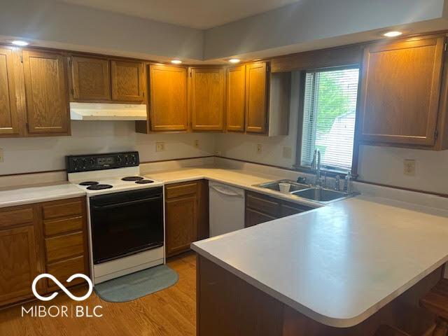 kitchen with white appliances, light countertops, brown cabinetry, a peninsula, and under cabinet range hood