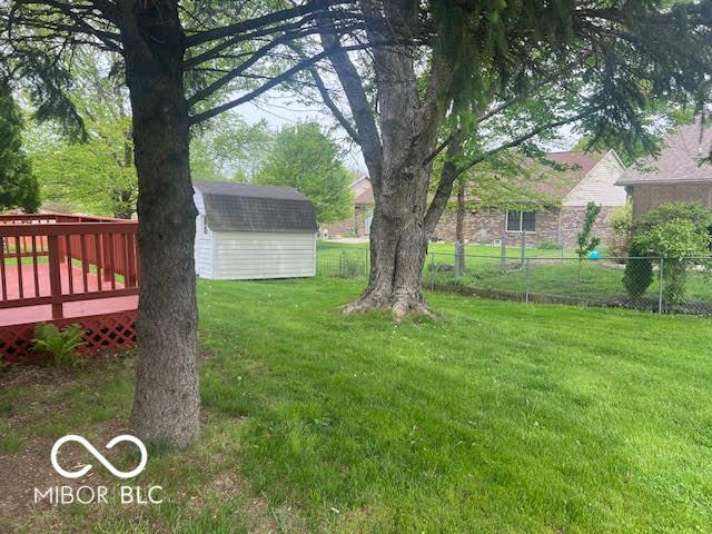 view of yard featuring a shed, an outbuilding, a deck, and fence