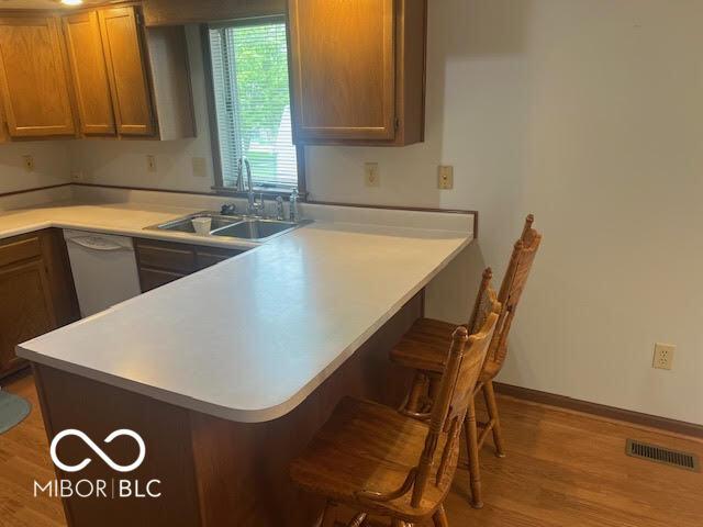 kitchen featuring a kitchen bar, visible vents, dishwasher, a sink, and a peninsula