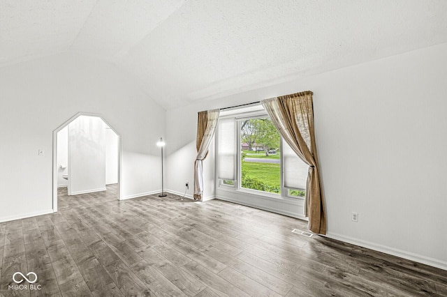 additional living space with visible vents, arched walkways, vaulted ceiling, wood finished floors, and baseboards