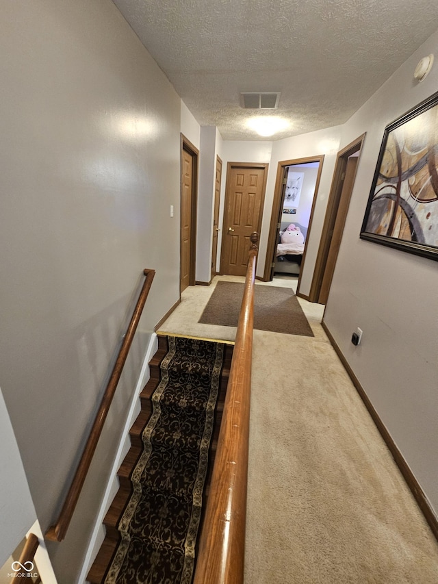 interior space featuring baseboards, carpet flooring, a textured ceiling, and visible vents