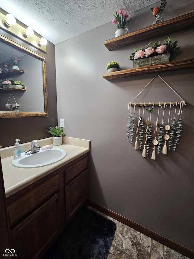 bathroom with vanity, baseboards, stone finish flooring, and a textured ceiling