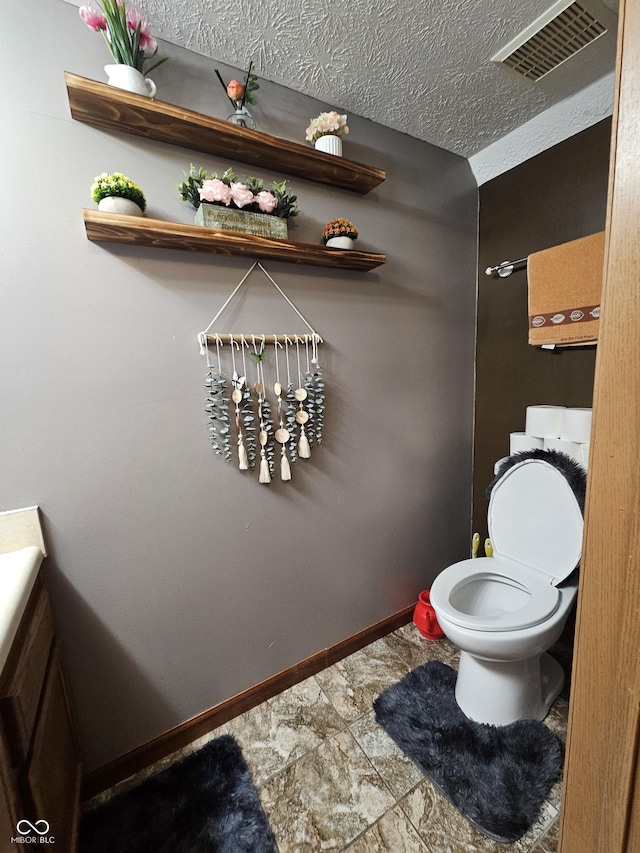 bathroom with toilet, a textured ceiling, visible vents, and baseboards