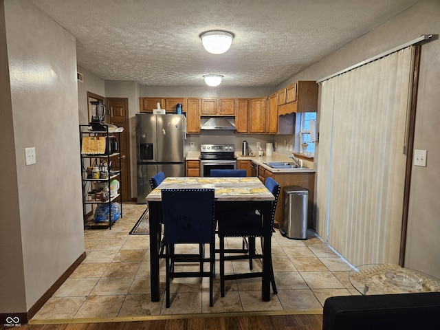 kitchen with brown cabinets, appliances with stainless steel finishes, a sink, light countertops, and under cabinet range hood