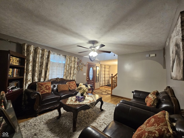 living room with stairs, a ceiling fan, a textured ceiling, and wood finished floors