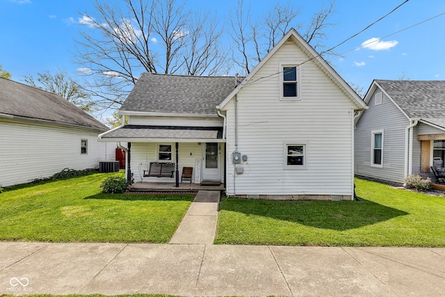 traditional-style house with roof with shingles, covered porch, central AC, and a front yard