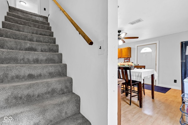 stairway featuring visible vents, a ceiling fan, baseboards, and wood finished floors