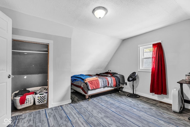 bedroom featuring baseboards, a textured ceiling, lofted ceiling, and wood finished floors