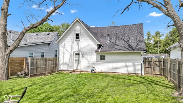 rear view of house featuring entry steps, a shingled roof, a yard, and a fenced backyard