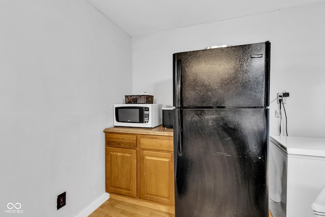 kitchen featuring fridge, light countertops, freestanding refrigerator, white microwave, and light wood-style floors