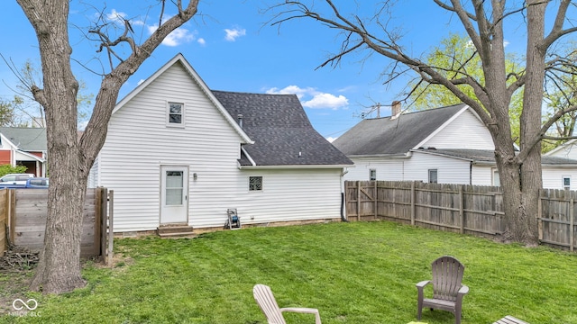 rear view of property with a lawn, roof with shingles, a fenced backyard, and entry steps