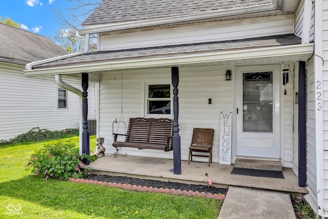 view of exterior entry with covered porch and a shingled roof
